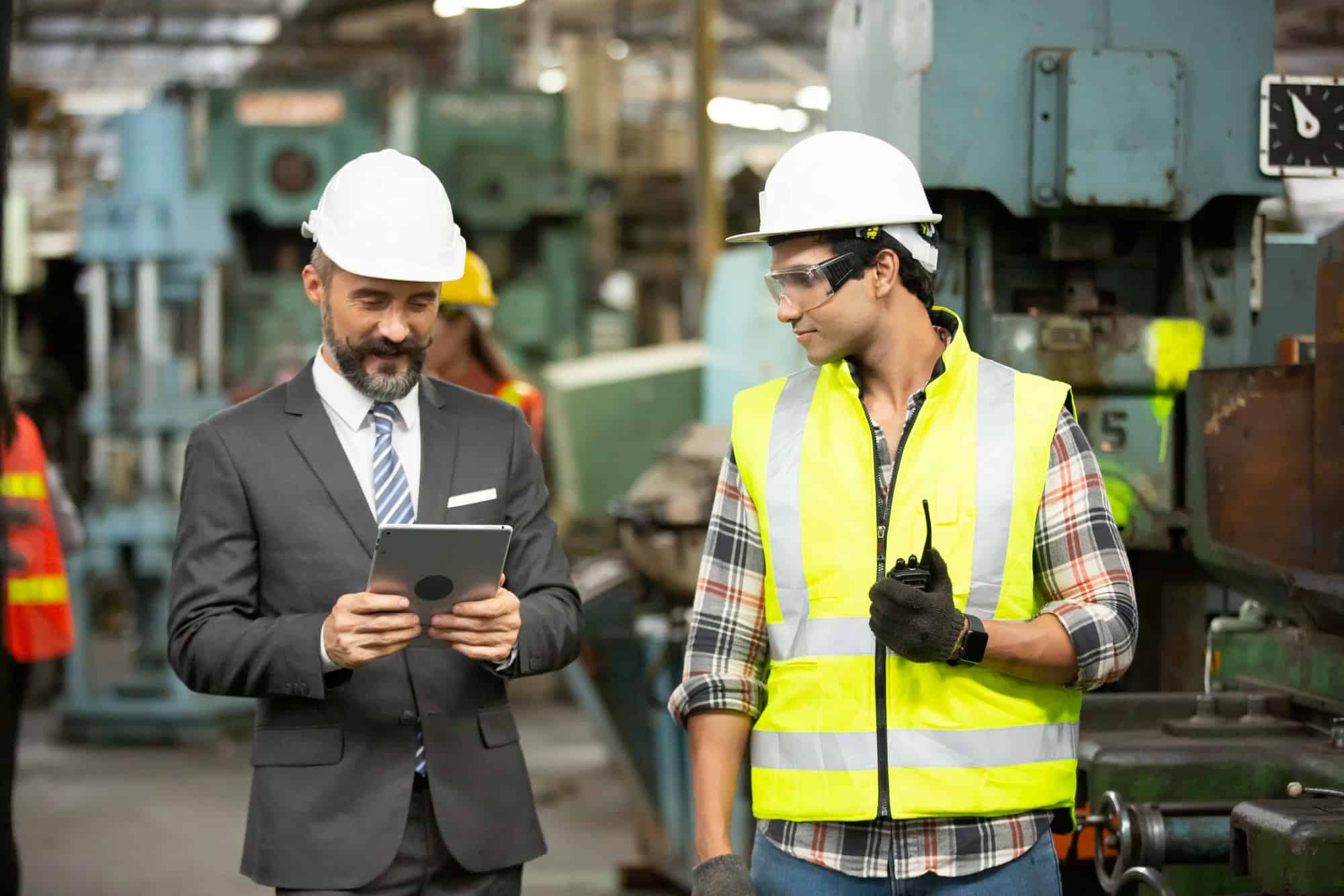 Two Heavy Industry Engineers Stand in Manufacturing Factory, Use Digital Tablet and discussing.